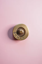 Gold fabric weight with 'Bunka' logo on a pink background